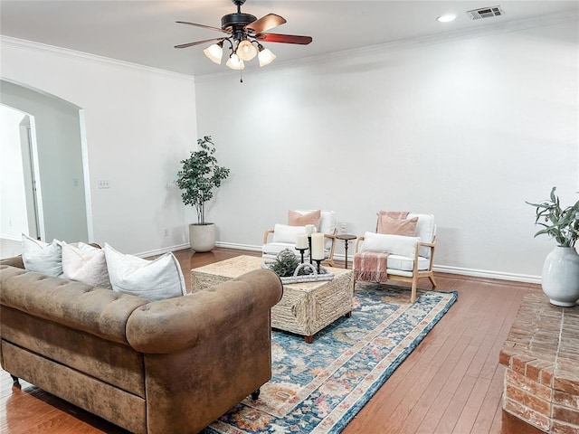 living room featuring arched walkways, visible vents, hardwood / wood-style floors, ornamental molding, and baseboards