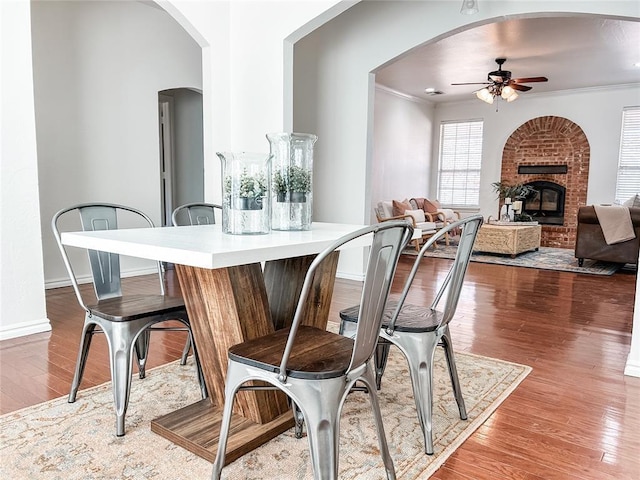 dining room with crown molding, a fireplace, a ceiling fan, wood finished floors, and baseboards