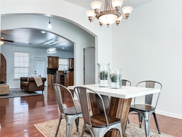 dining space featuring dark wood-style floors, baseboards, arched walkways, and ceiling fan with notable chandelier