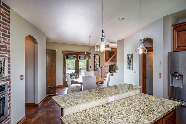 kitchen featuring a center island, arched walkways, appliances with stainless steel finishes, baseboards, and light stone countertops