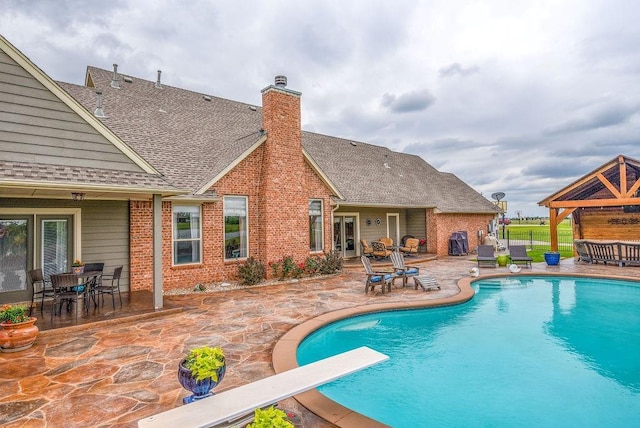 outdoor pool with a patio, outdoor dining area, french doors, and a diving board