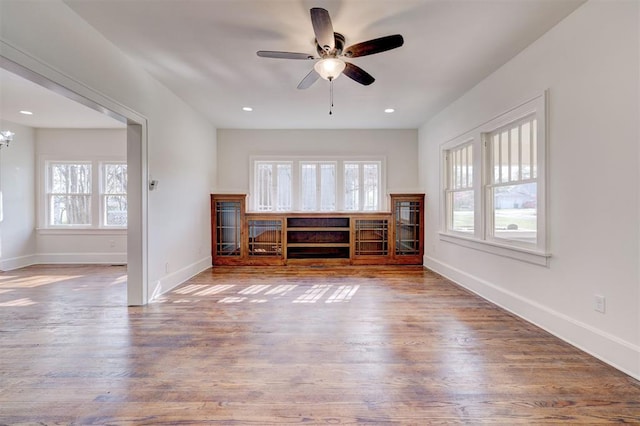 unfurnished living room featuring baseboards, plenty of natural light, wood finished floors, and ceiling fan with notable chandelier