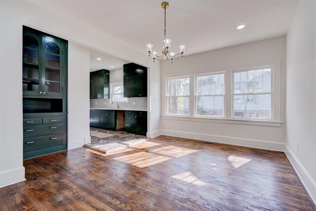 unfurnished living room with a notable chandelier, baseboards, recessed lighting, a sink, and wood finished floors