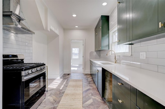 kitchen featuring gas stove, wall chimney range hood, light countertops, a healthy amount of sunlight, and a sink