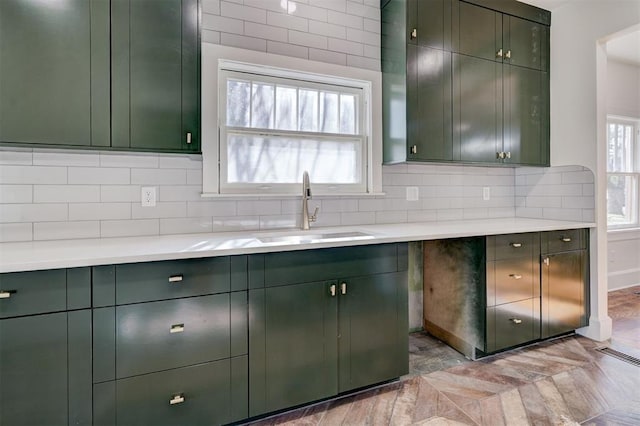kitchen with visible vents, green cabinetry, a sink, light countertops, and backsplash