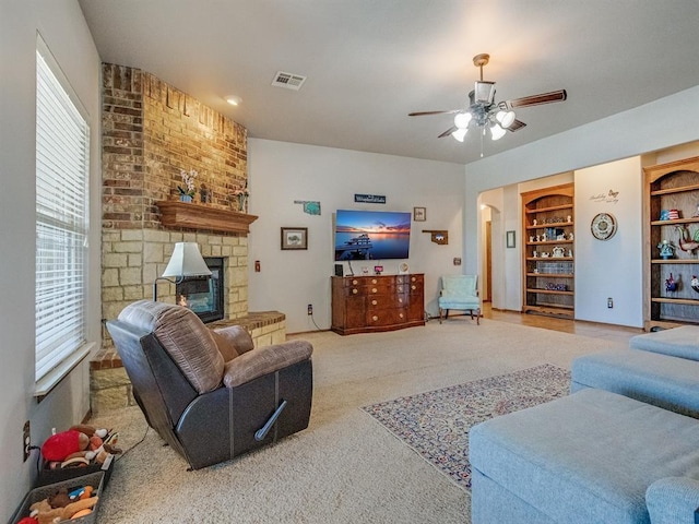 living area with visible vents, arched walkways, a ceiling fan, a stone fireplace, and built in shelves