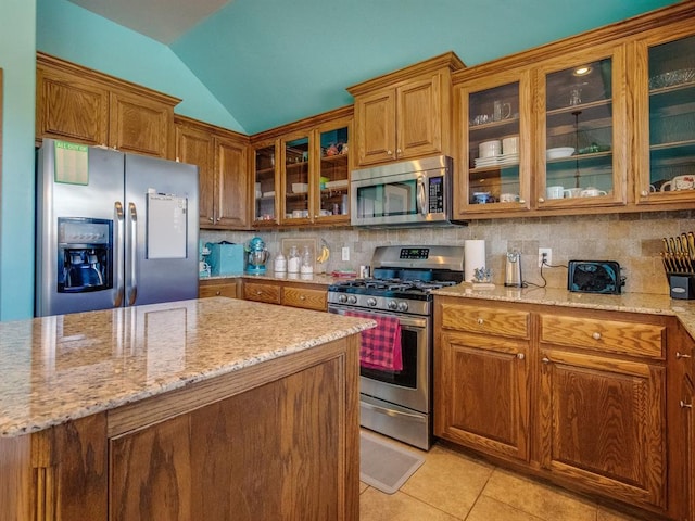 kitchen featuring glass insert cabinets, appliances with stainless steel finishes, brown cabinetry, and decorative backsplash