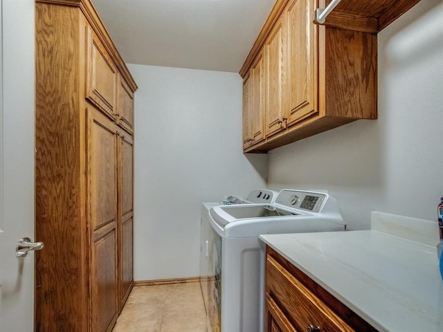 laundry area featuring light tile patterned flooring, washing machine and dryer, cabinet space, and baseboards