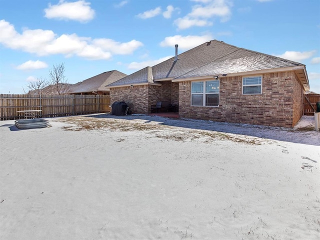 snow covered rear of property with a shingled roof, fence, and brick siding