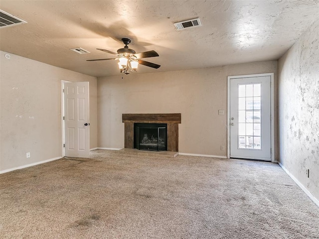 unfurnished living room featuring carpet floors, visible vents, a fireplace with raised hearth, and a ceiling fan