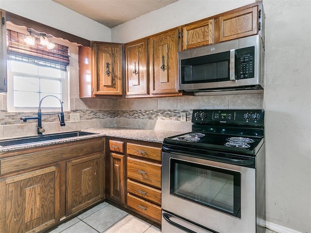 kitchen featuring light tile patterned floors, a sink, appliances with stainless steel finishes, backsplash, and brown cabinets