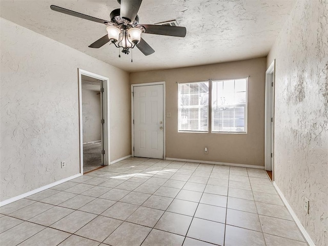 spare room featuring a textured ceiling, a textured wall, light tile patterned flooring, and baseboards