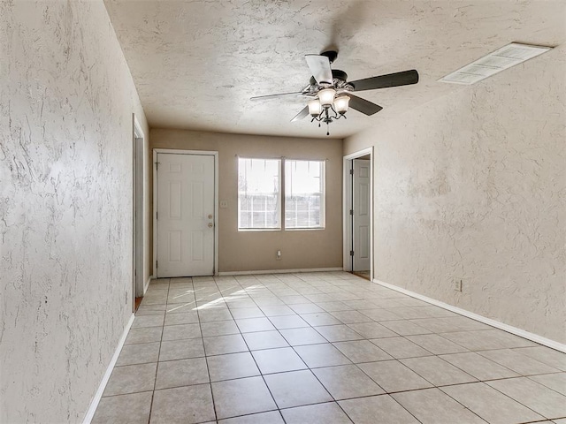 empty room featuring baseboards, visible vents, a textured wall, a textured ceiling, and light tile patterned flooring