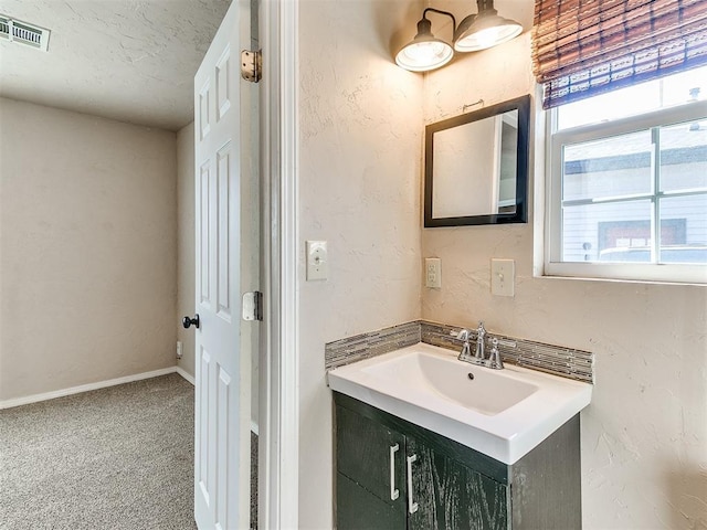 bathroom with a textured wall, vanity, visible vents, and baseboards