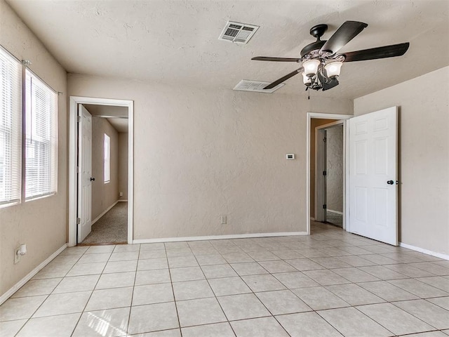 empty room with light tile patterned floors, visible vents, a textured wall, ceiling fan, and baseboards