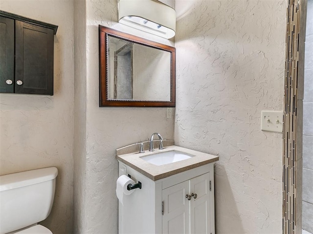 half bath featuring a textured wall, vanity, and toilet