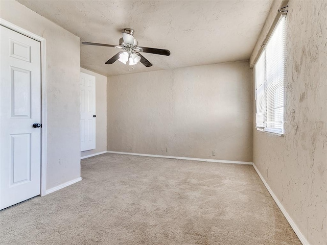 carpeted spare room with a ceiling fan, a textured wall, and baseboards