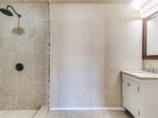 bathroom featuring a tile shower, vanity, and baseboards