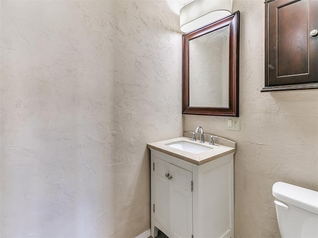 half bath with a textured wall, vanity, and toilet