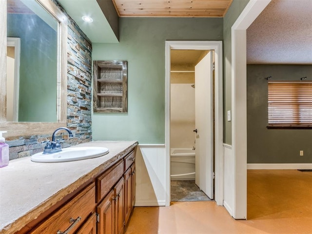 bathroom with vanity, finished concrete flooring, bathtub / shower combination, a wainscoted wall, and baseboards