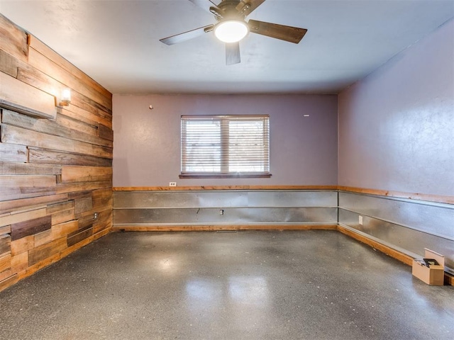 empty room with wooden walls, ceiling fan, and speckled floor