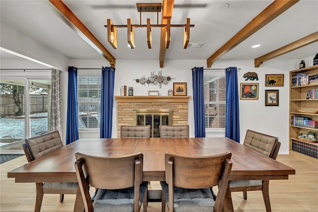 dining room featuring light wood-type flooring, visible vents, a fireplace, and beamed ceiling