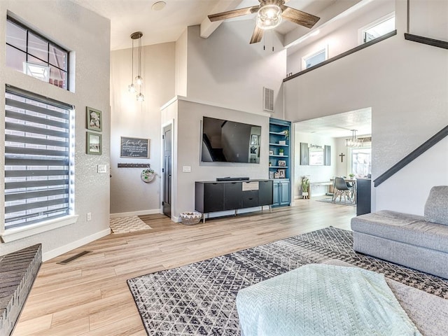 living area with ceiling fan with notable chandelier, visible vents, baseboards, and wood finished floors