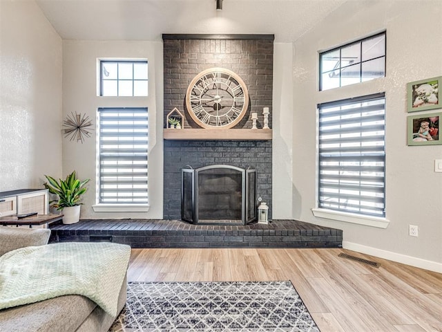 living room with a brick fireplace, baseboards, visible vents, and wood finished floors