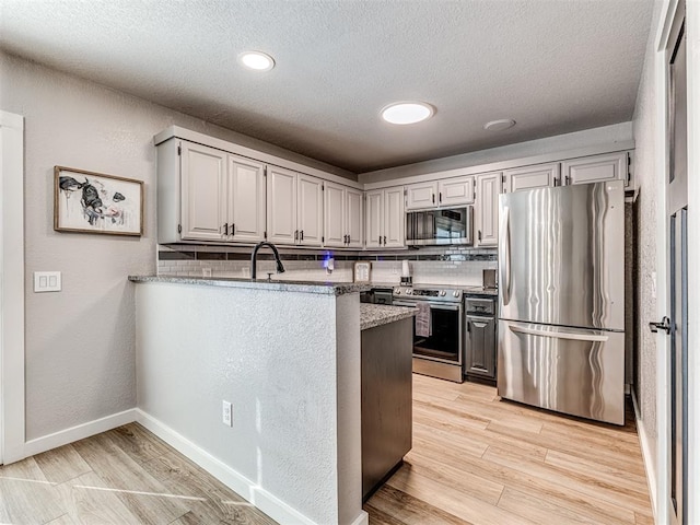 kitchen with appliances with stainless steel finishes, light wood-style flooring, a peninsula, and tasteful backsplash