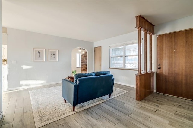 living area with arched walkways, baseboards, and light wood-style floors