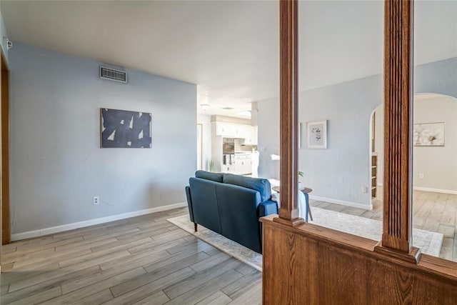 interior space with arched walkways, wood finished floors, visible vents, baseboards, and decorative columns