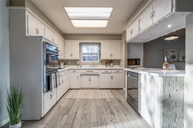 kitchen with light wood-style flooring, white cabinetry, light countertops, backsplash, and black appliances