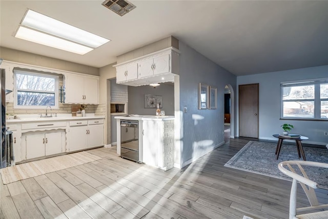 kitchen with visible vents, arched walkways, white cabinets, dishwasher, and light countertops