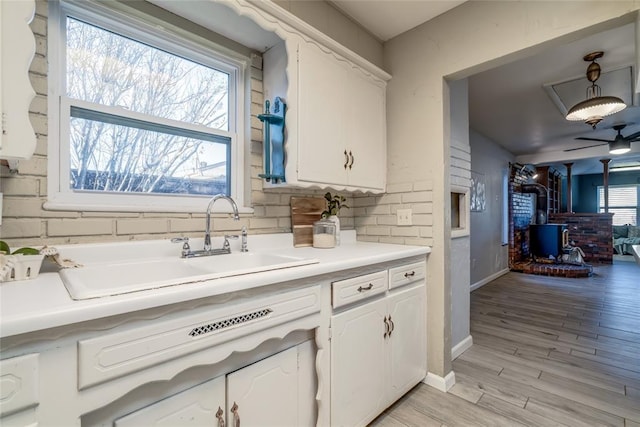 kitchen featuring a sink, baseboards, white cabinets, light countertops, and light wood finished floors