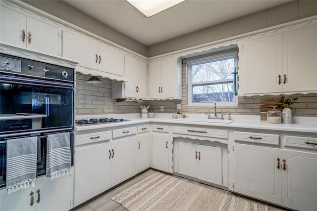 kitchen featuring dobule oven black, gas stovetop, white cabinetry, and a sink