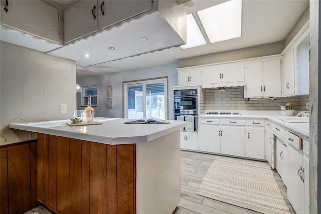 kitchen with a sink, light countertops, backsplash, and white cabinetry