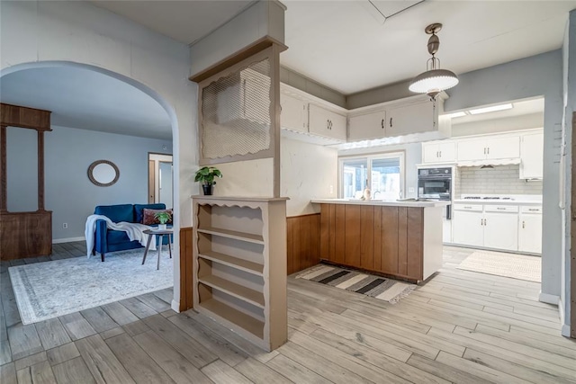 kitchen with arched walkways, a peninsula, light wood-style floors, backsplash, and stovetop