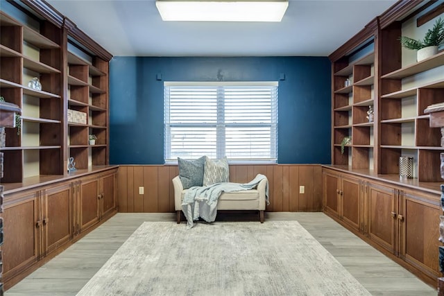 living area with light wood finished floors, a skylight, wood walls, and wainscoting