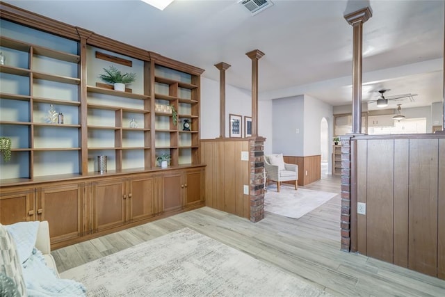 living area featuring arched walkways, visible vents, a ceiling fan, wainscoting, and light wood finished floors