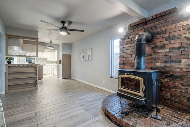 living room with beam ceiling, a ceiling fan, a wood stove, light wood-type flooring, and baseboards