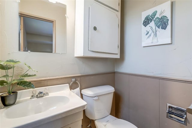 half bath with wainscoting, vanity, and toilet