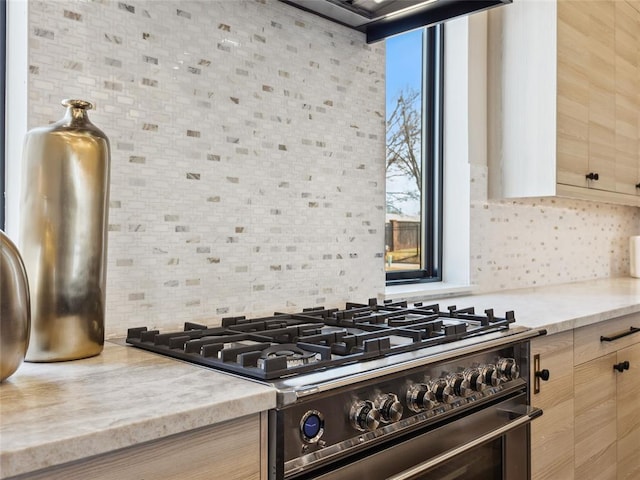 kitchen with light brown cabinetry, tasteful backsplash, high end stainless steel range, and light stone counters