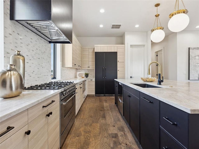 kitchen with visible vents, light brown cabinetry, high end stove, wall chimney range hood, and a sink