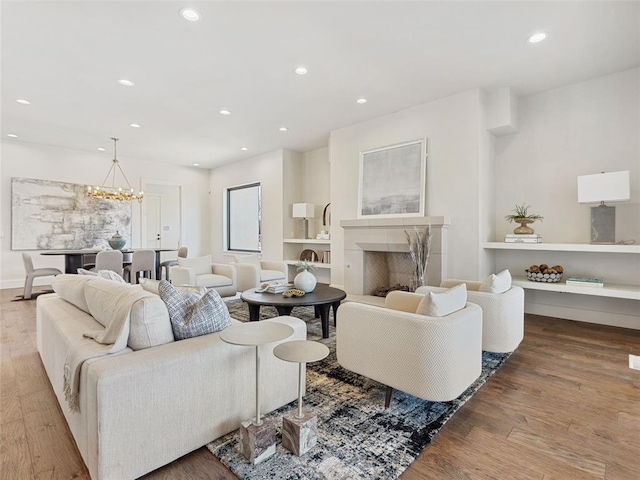 living area with recessed lighting, a fireplace, an inviting chandelier, and wood finished floors