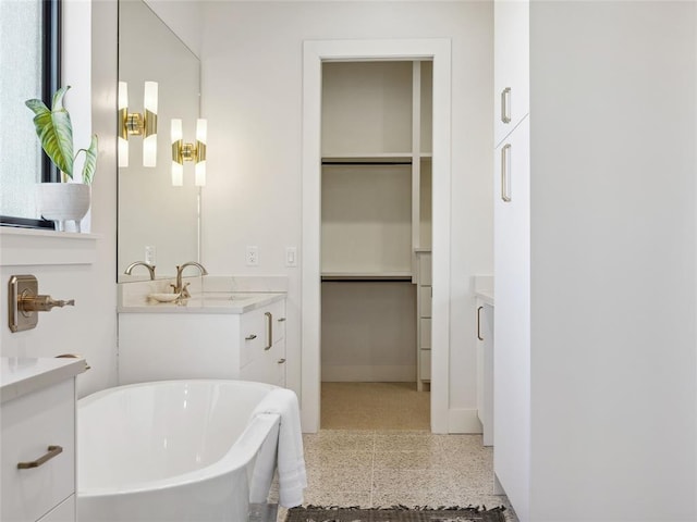 bathroom with a freestanding bath, speckled floor, a walk in closet, and vanity