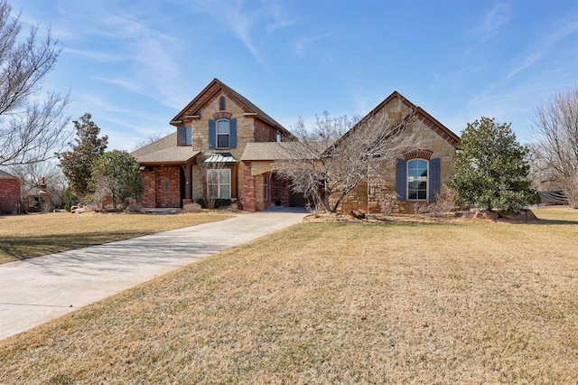 traditional-style house featuring a front yard, stone siding, and driveway