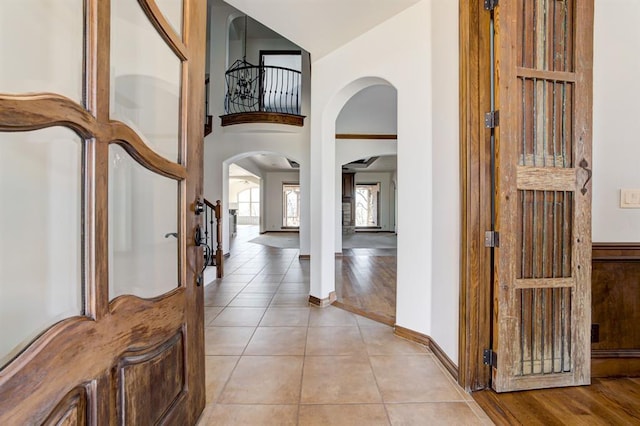 foyer featuring arched walkways, a towering ceiling, baseboards, and light tile patterned floors