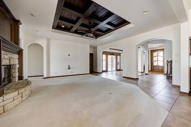 unfurnished living room featuring light tile patterned floors, a stone fireplace, coffered ceiling, and baseboards