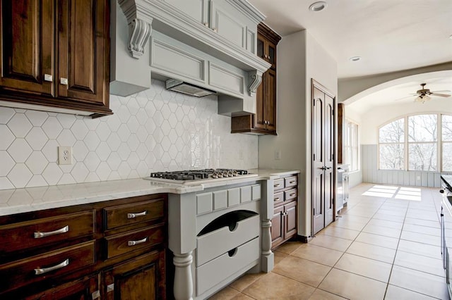 kitchen with light stone counters, stainless steel gas cooktop, glass insert cabinets, light tile patterned flooring, and ceiling fan