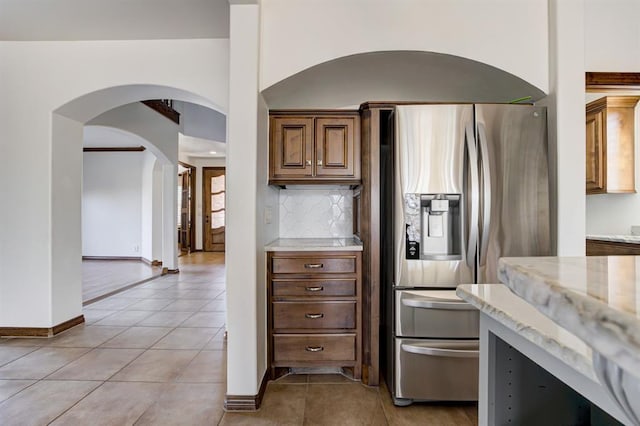 kitchen with light tile patterned floors, tasteful backsplash, stainless steel fridge with ice dispenser, light stone countertops, and baseboards